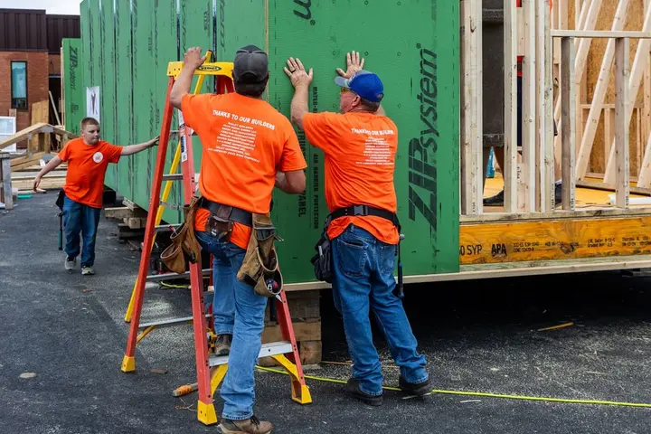 AHBA volunteers in orange Thanks to Our Builders shirts raising a wall panel at a community build